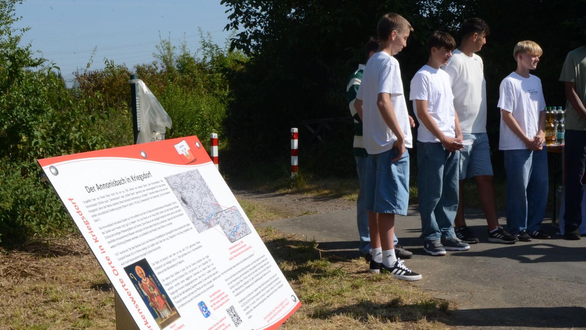 Eine Schautafel mit der Überschrift „Der Annonisbach in Kriegsdorf“. Im Hintergrund stehen Schüler.