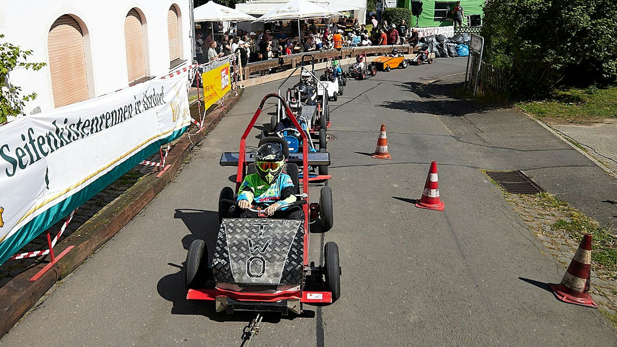 Seifenkisten werden am Seil gezogen und bilden eine lange Kette am Start. Im Hintergrund sind Zuschauer zu sehen.