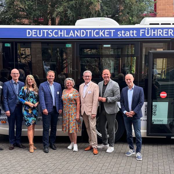 Das Foto zeigt eine Gruppe von Männern und Frauen vor einem Bus mit der Aufschrift „Deutschlandticket statt Führerschein“: