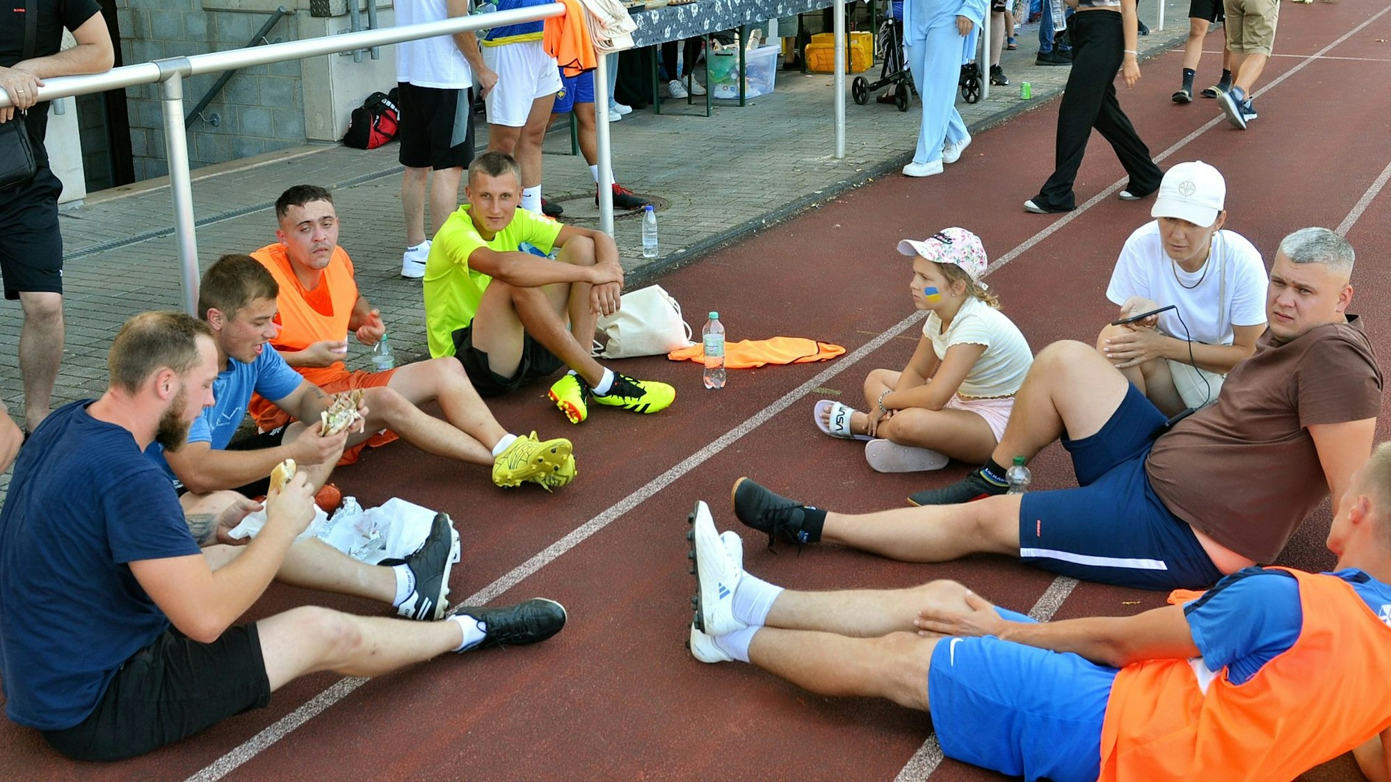 Mehrere Männer und ein Mädchen sitzen auf der Laufbahn im Stadion.