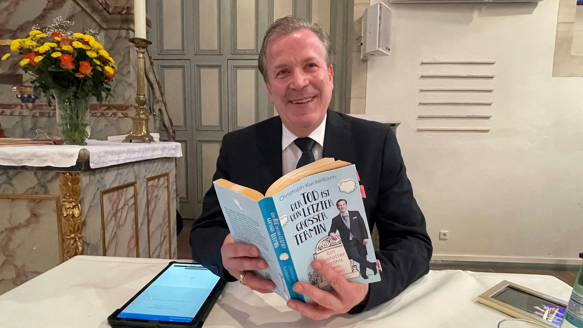 Christoph Kuckelkorn hält das Buch „Der Tod ist dein letzter großer Termin“ in Händen.