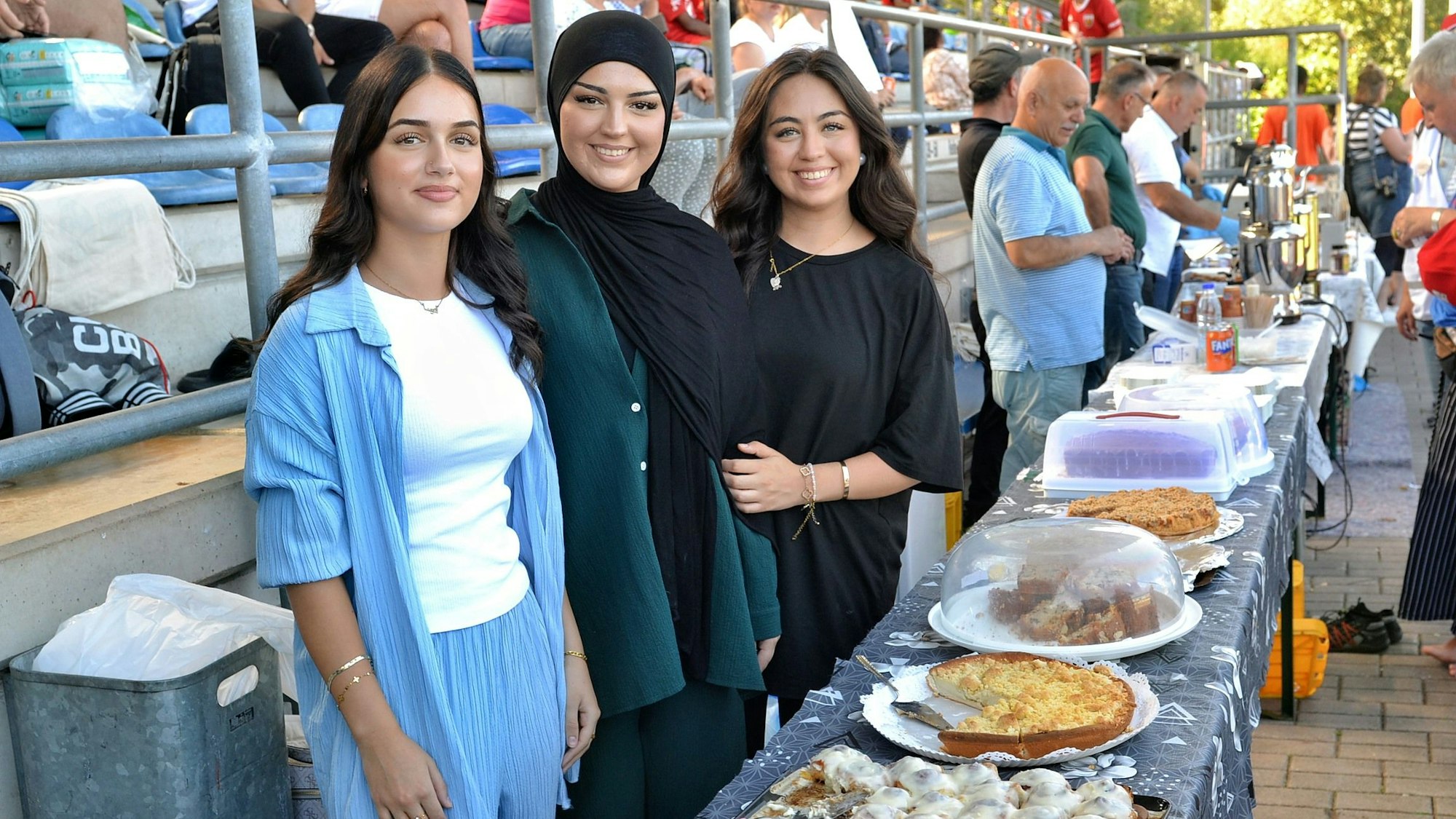 Drei junge Frauen stehen hinter einem Tisch, auf dem Kuchen stehen.
