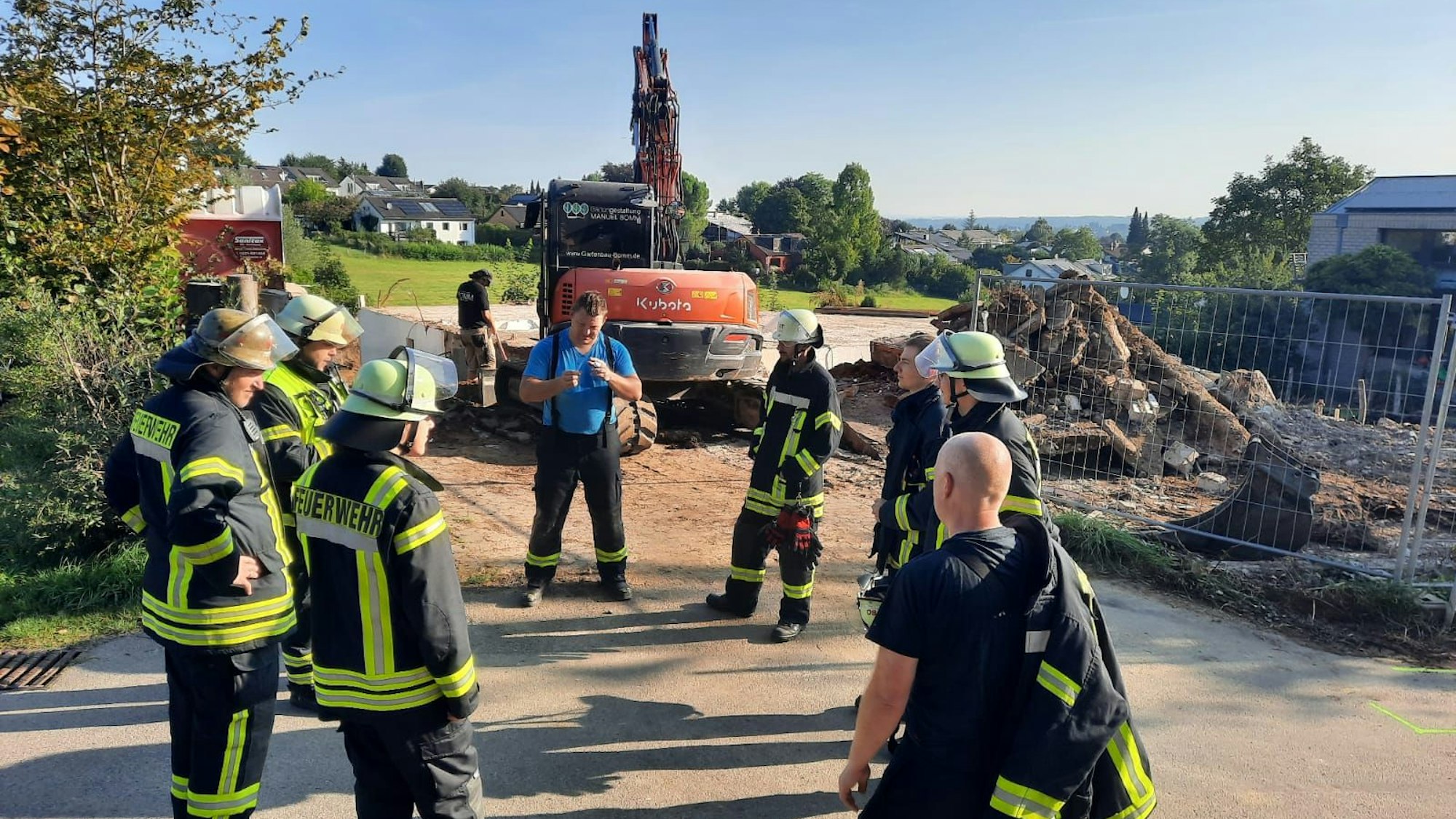 Mehrere Feuerwehrleute vor einem Abrissbagger.