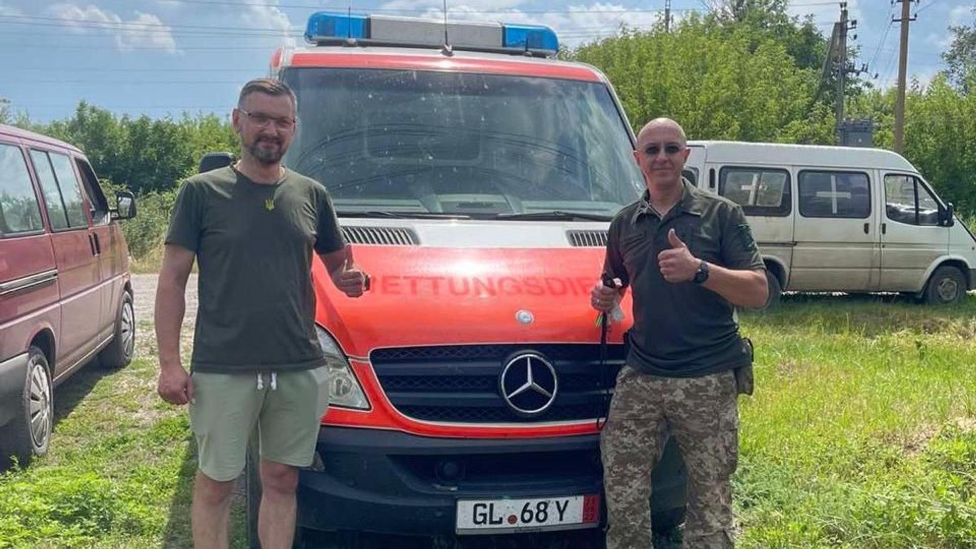 zwei Männer stehen vor einem Krankenwagen und strecken den Daumen in die Höhe.