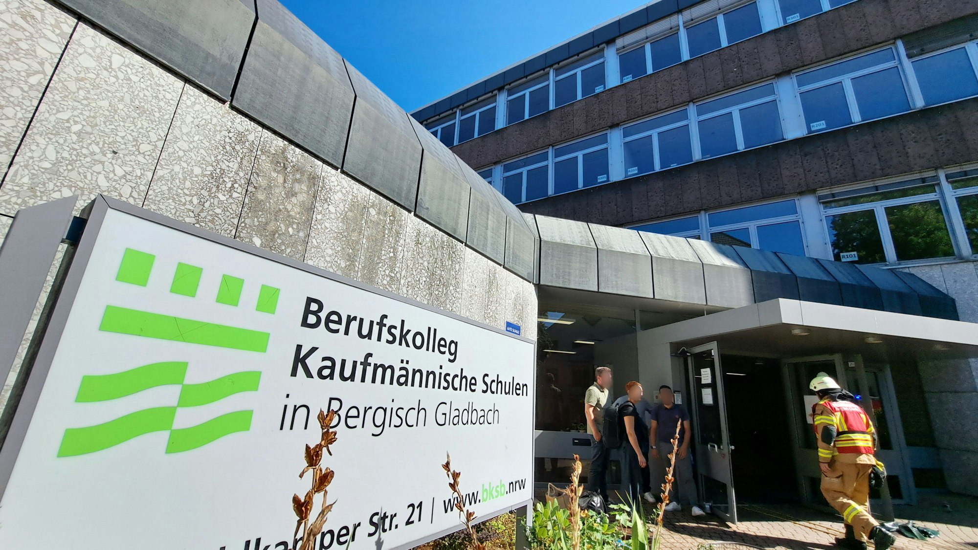 Zwei Feuerwehrleute gehen ins Berufskolleg Kaufmännische Schulen an der Oberheidkamper Straße in Bergisch Gladbach.