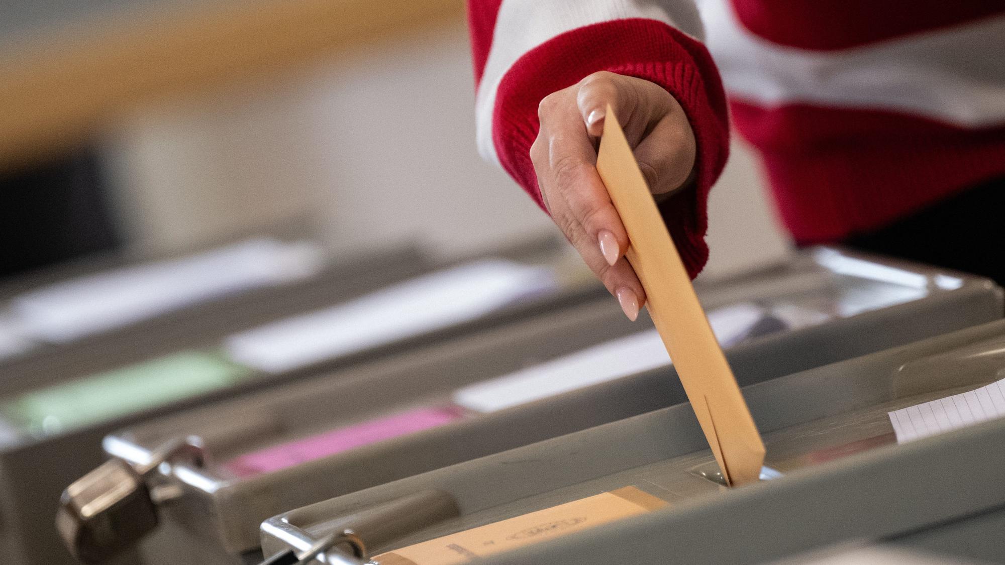 Eine Wählerin wirft in einem Wahlraum einen Wahlschein in eine Urne.