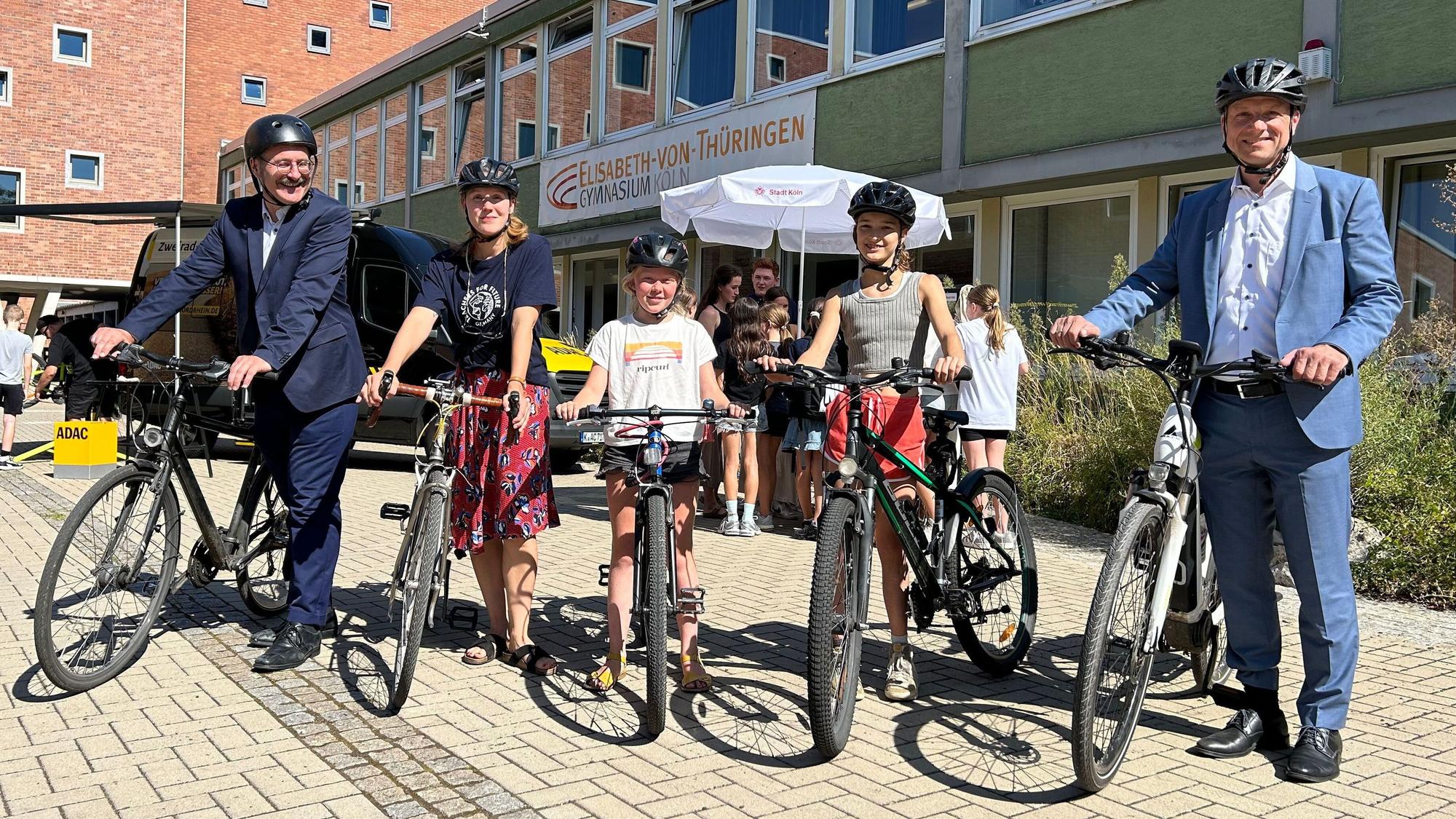 Fünf Personen stehen mit ihren Fahrrädern auf einem Schulhof.