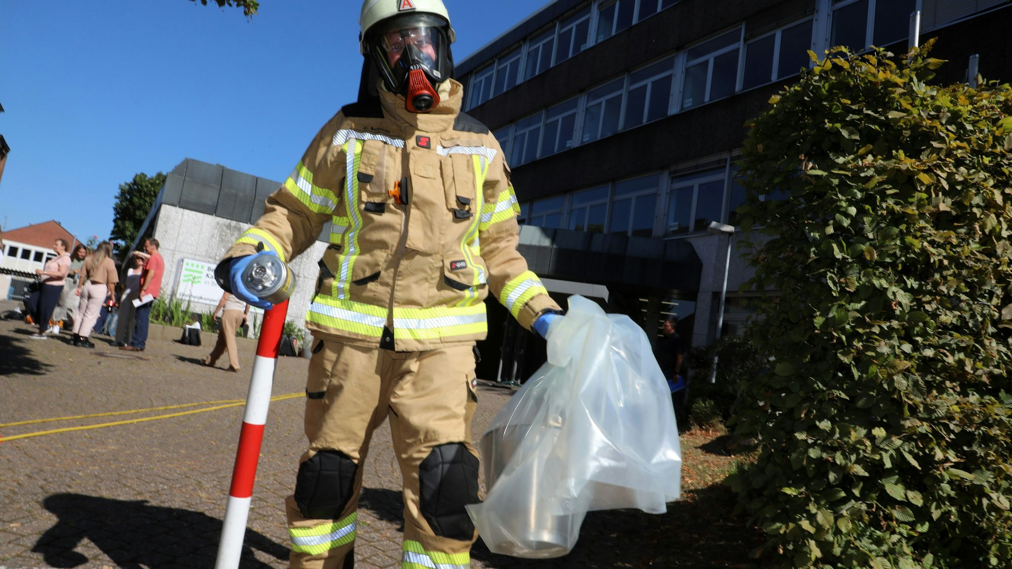 Ein Feuerwehrmann mit Atemschutzmaske trägt eine Kunststofftüte mit gefährlichen Substanz aus dem Berufskolleg Kaufmännische Schulen in Bergisch Gladbach-Heidkamp ins Freie.