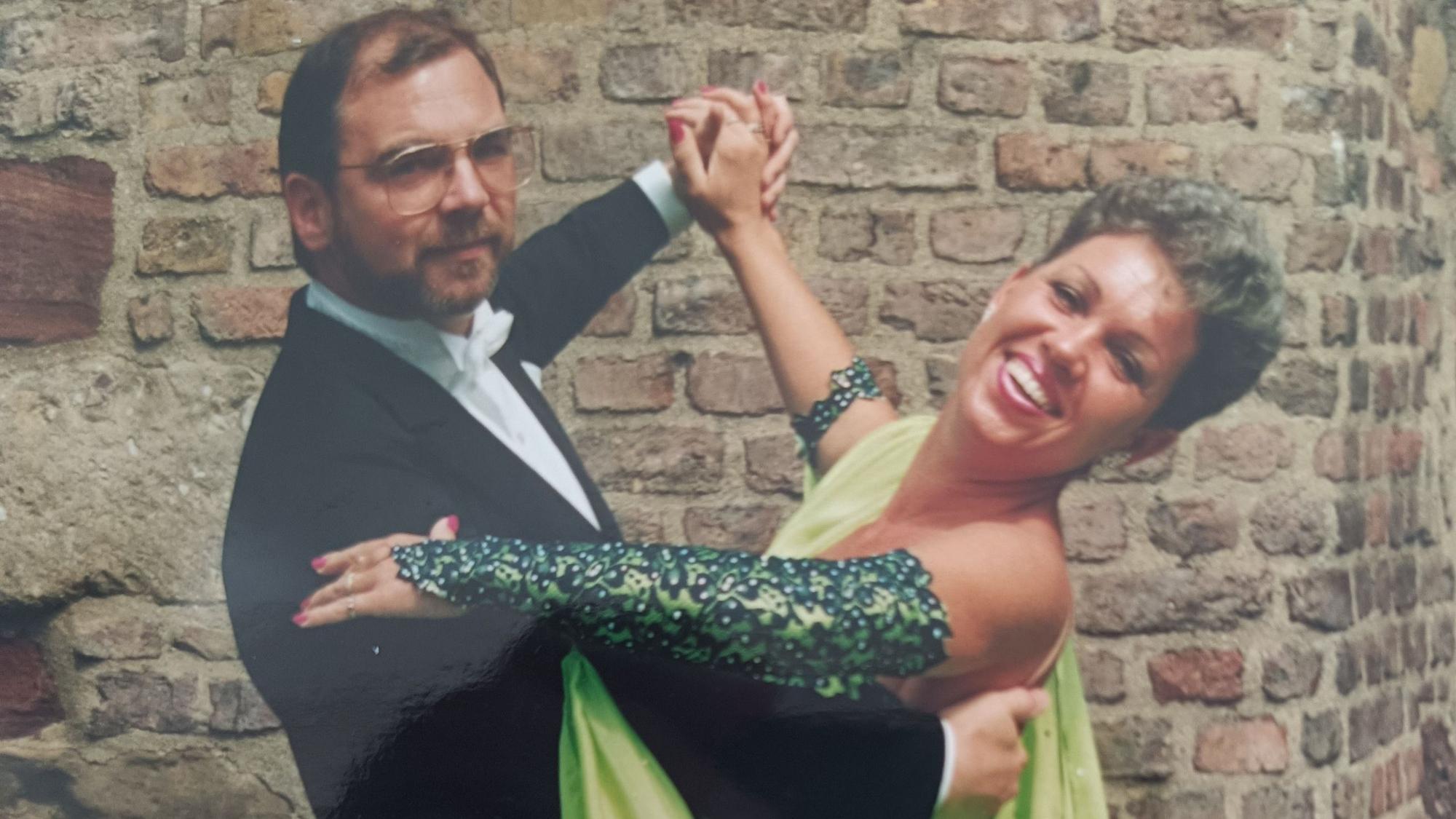 Die beiden tanzen gemeinsam. Jutta Zodet trägt ein grünes Kleid, Ralf Zodet trägt einen Frack und eine eckige Brille.