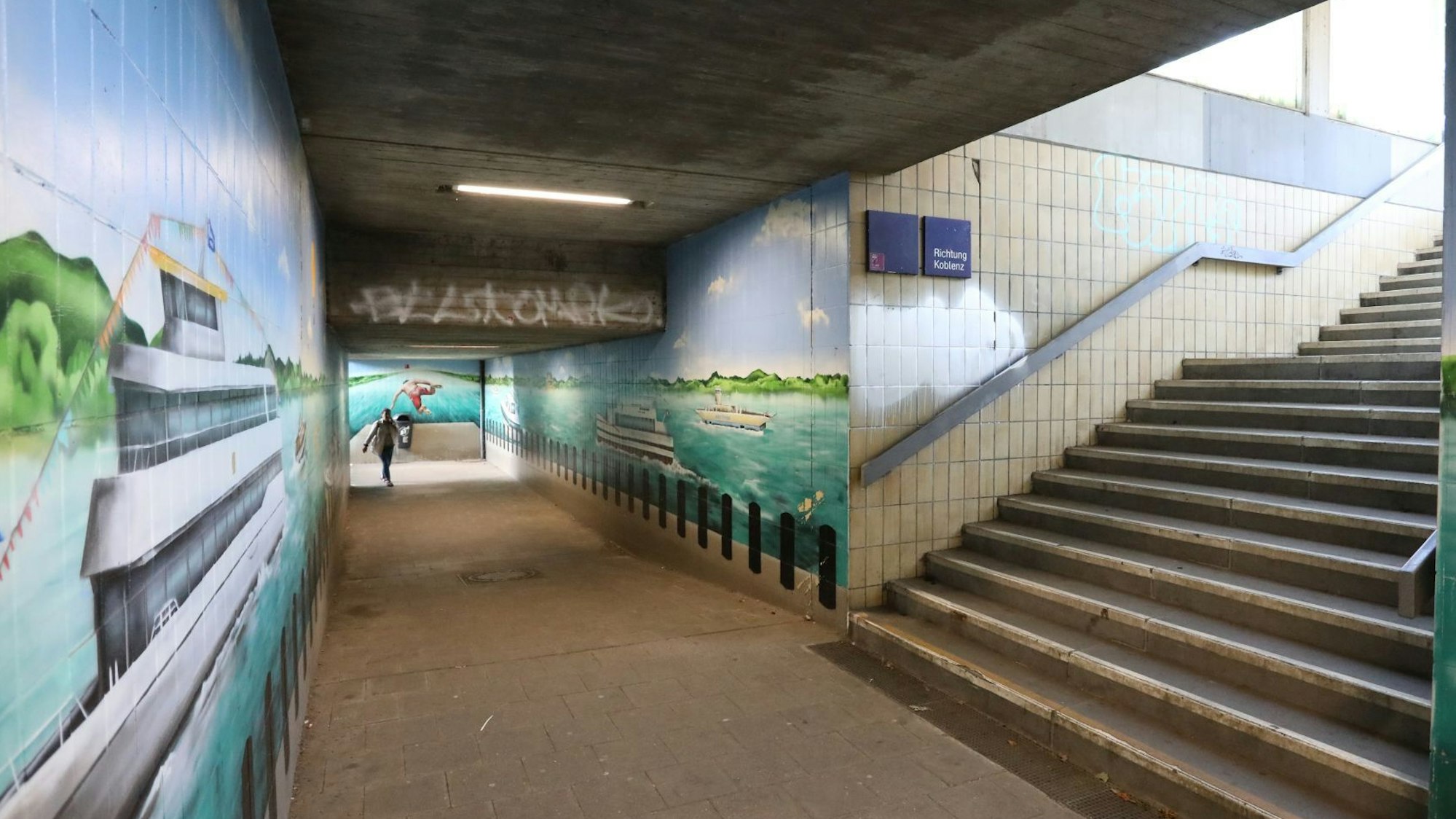 Eine Fußgängerunterführung, an den Wänden sind Bilder gemalt, die Schiffe auf dem Rhein zeigen.