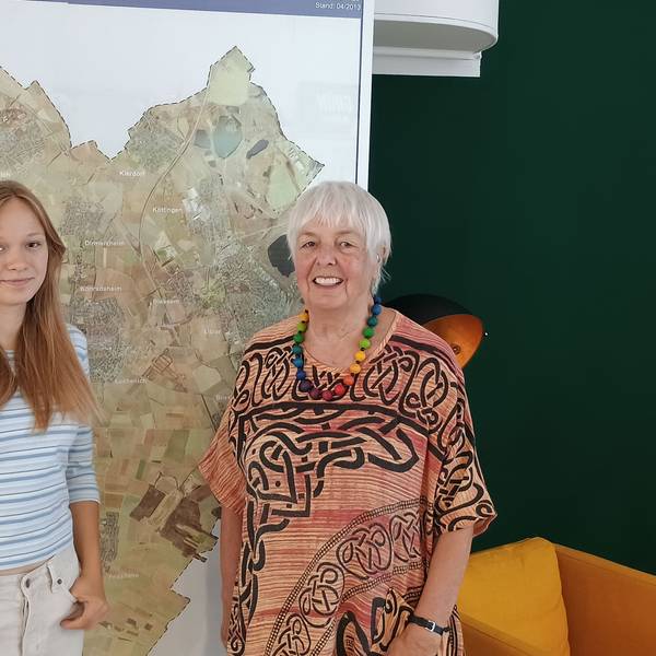 Lena conrady trägt ein weißes Top mit blauen Streifen. Elke Griemens trägt ein rötliches Kleid mit auffälligen Mustern und eine bunte Perlenkette. Hinter den beiden hängt eine große Karte von Erftstadt.