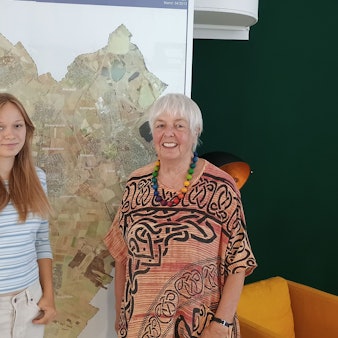 Lena conrady trägt ein weißes Top mit blauen Streifen. Elke Griemens trägt ein rötliches Kleid mit auffälligen Mustern und eine bunte Perlenkette. Hinter den beiden hängt eine große Karte von Erftstadt.