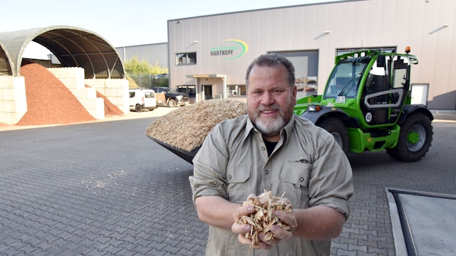 Ein Forstunternehmer steht auf einem Hof, im Hintergrund eine Forstmaschine.