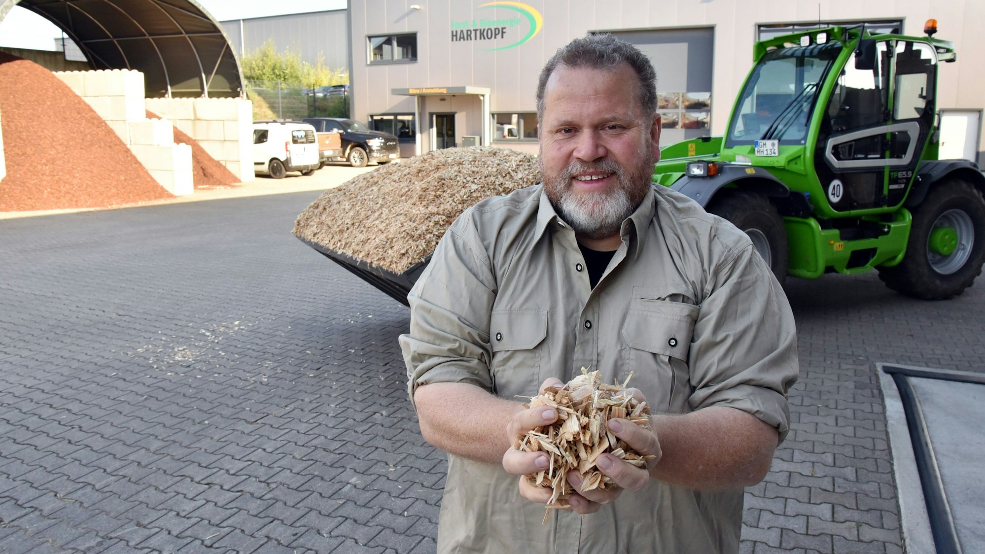 Ein Forstunternehmer steht auf einem Hof, im Hintergrund eine Forstmaschine.