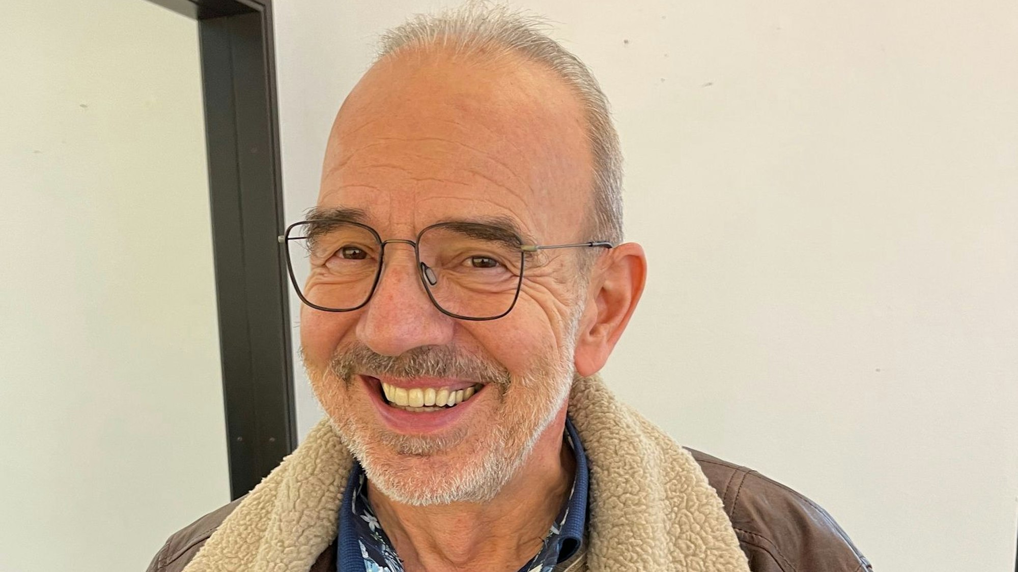 Ein Mann in geöffneter Lederjacke und Pullover lächelt in die Kamera.