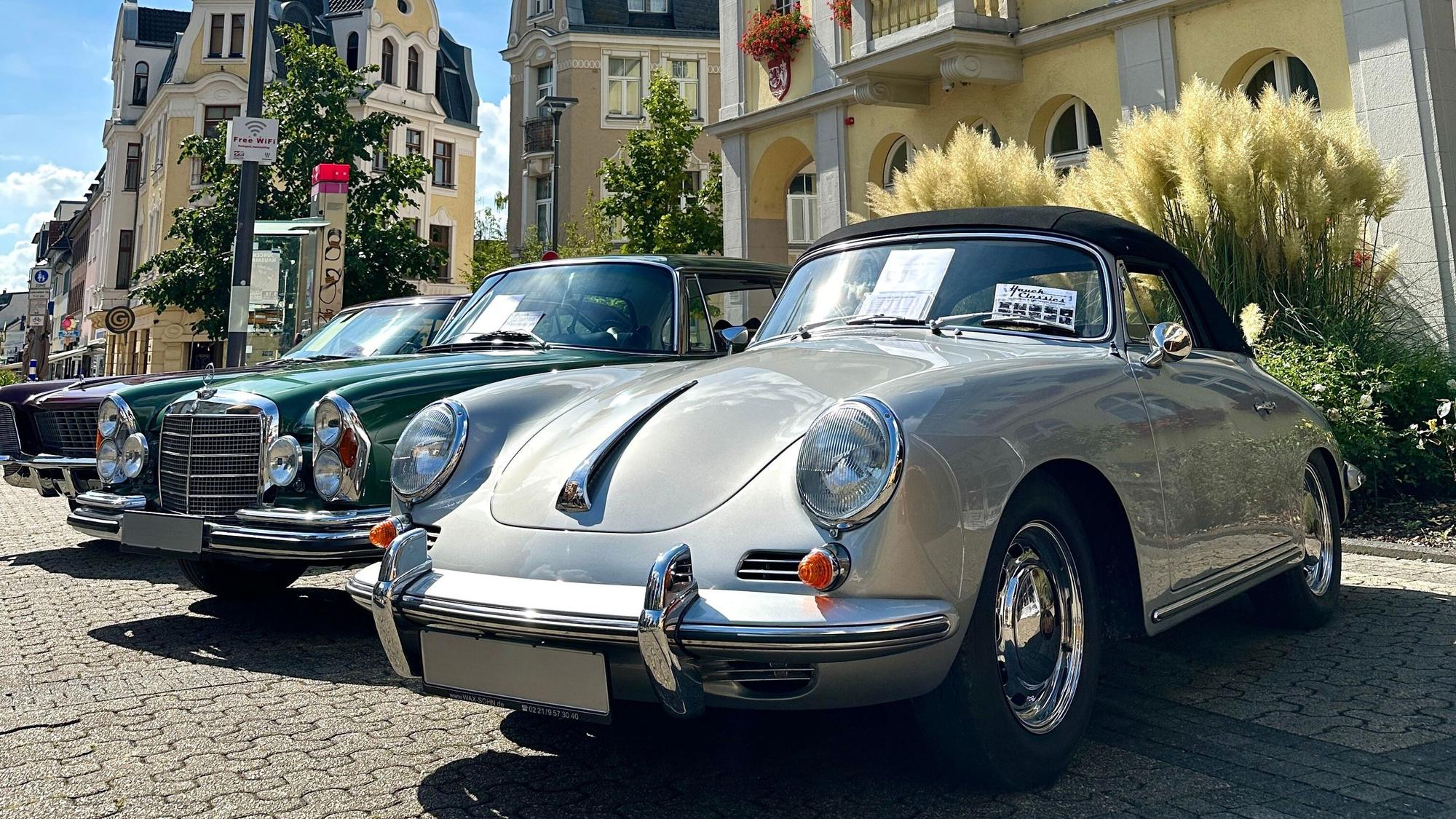 Auf dem Bild sind ein grüner und ein grauer Oldtimer zu sehen.