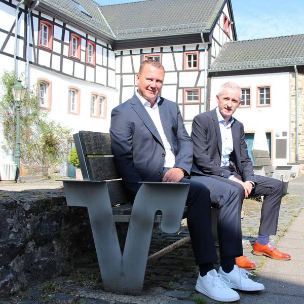 Mark Heiter und Kai Zinken sitzen auf einer Bank. Im Hintergrund sind Blankenheimer Fachwerkhäuser zu sehen.