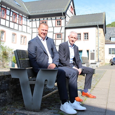 Mark Heiter und Kai Zinken sitzen auf einer Bank. Im Hintergrund sind Blankenheimer Fachwerkhäuser zu sehen.