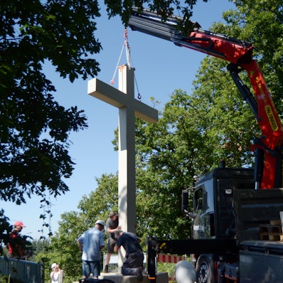 Das Betonkreuz hängt an einem Ladekran. Mitarbeiter der Baufirma bringen es in Position.