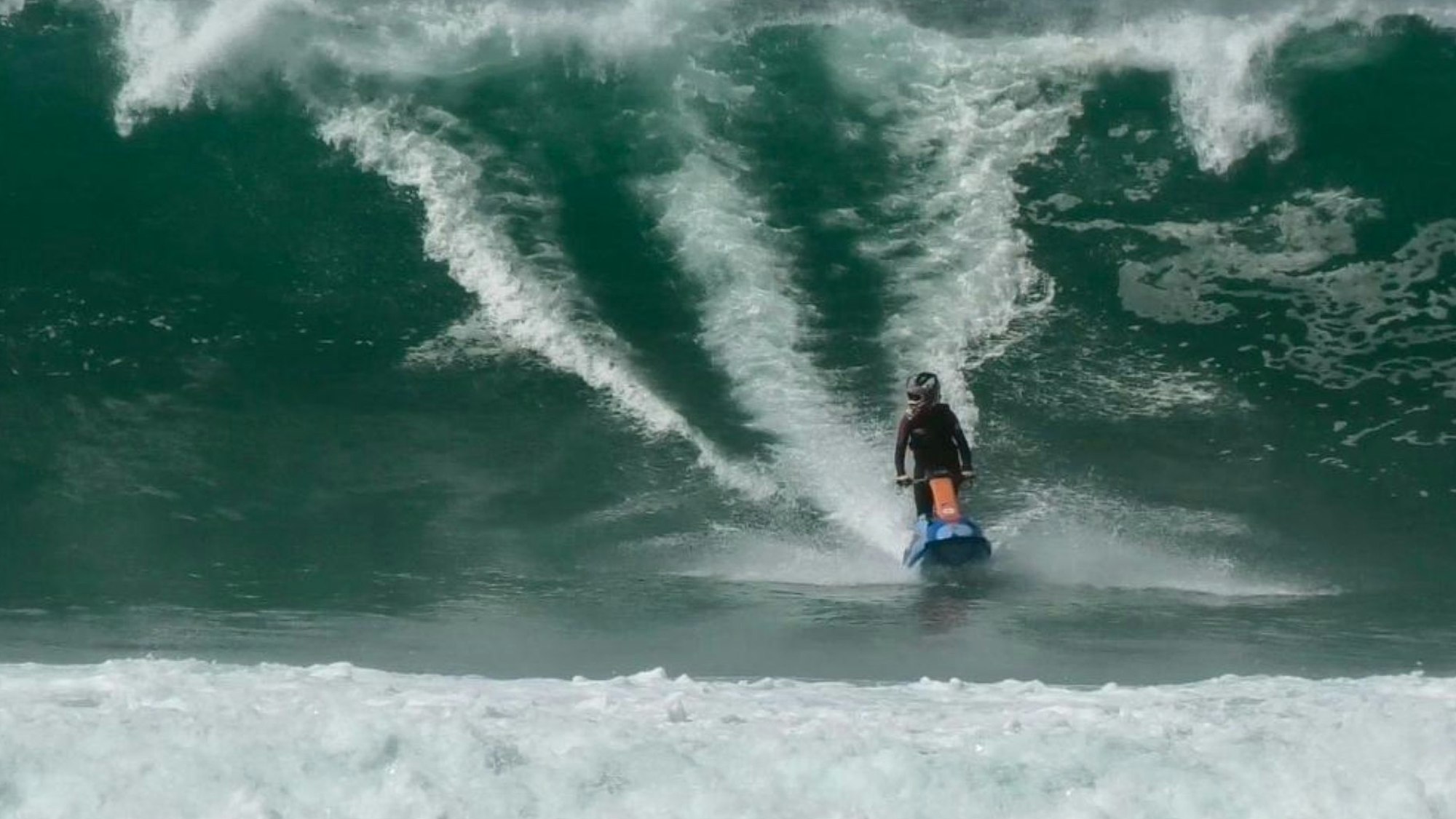 Eine junge Frau fährt mit ihrem Jetski in der Meeresbrandung vor der französischen Küste vor einer hohen Welle.