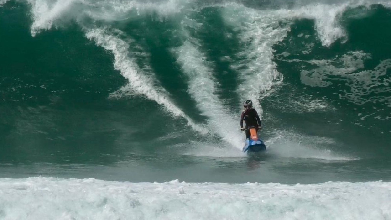 Eine junge Frau fährt mit ihrem Jetski in der Meeresbrandung vor der französischen Küste vor einer hohen Welle.