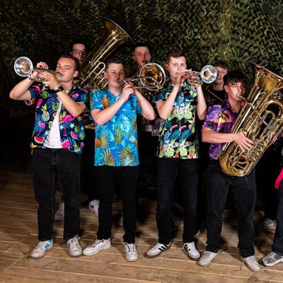 Zehn junge Musiker mit Blechblasinstrumenten stehen in einer Gruppe zusammen und tragen bunte Hawaiihemden.