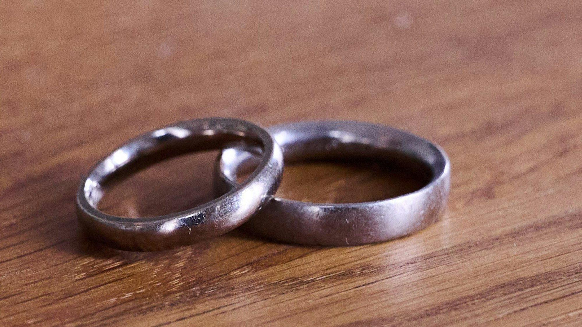 Ein Paar Eheringe liegt auf einem Holztisch.