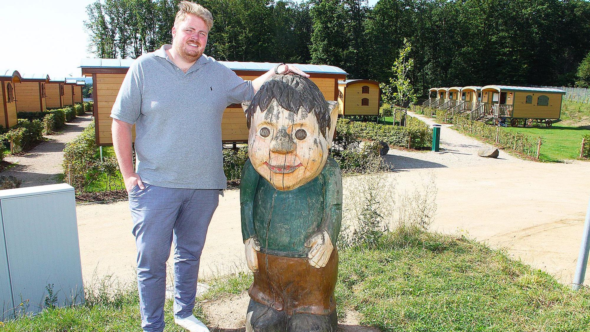 Lars-Hendrik Harsveld steht vor zahlreichen gelben Bauwagen neben einer Holzfigur.