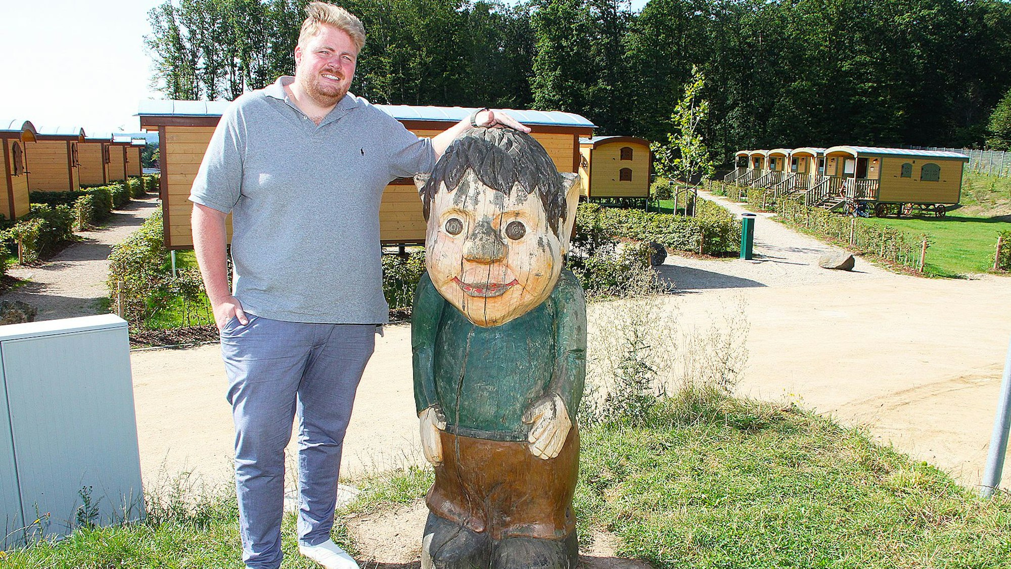 Lars-Hendrik Harsveld steht vor zahlreichen gelben Bauwagen neben einer Holzfigur.