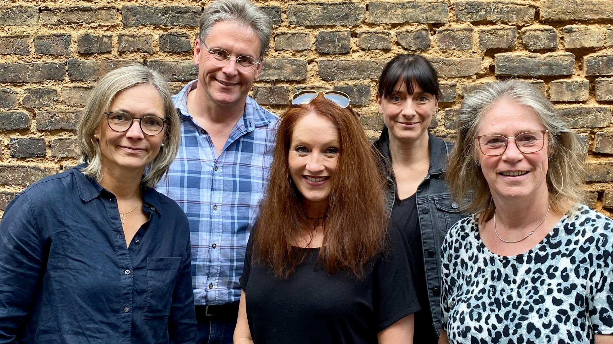 Die Teammitglieder haben sich zum Gruppenfoto vor einer braunen Mauer aufgestellt.