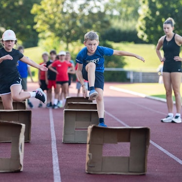 Kinder üben Hürdenlauf mit aufgestellten Pappkartons.
