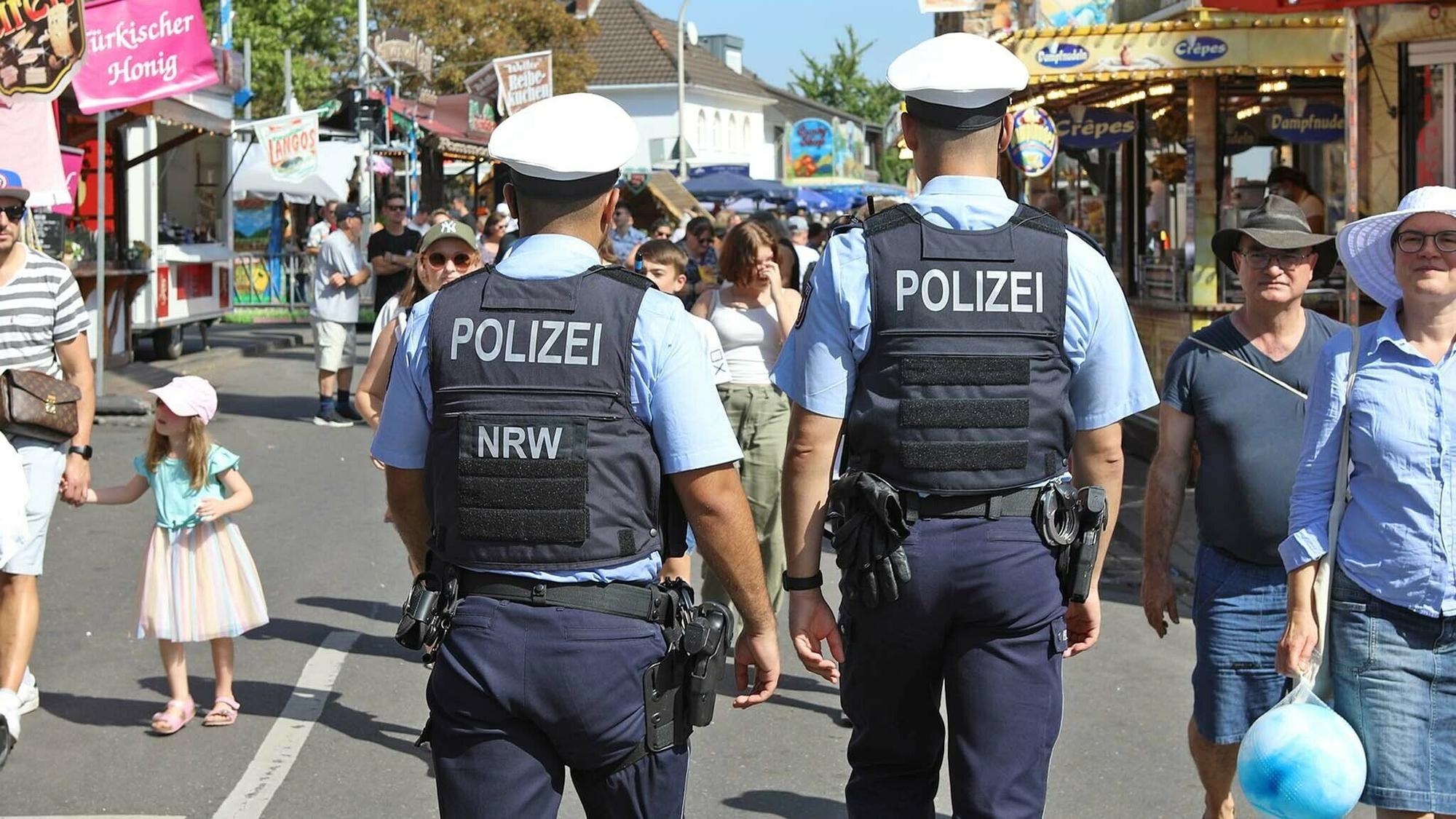 Zwei Polizisten gehen über eine Straße auf der Kirmesbuden stehen.
