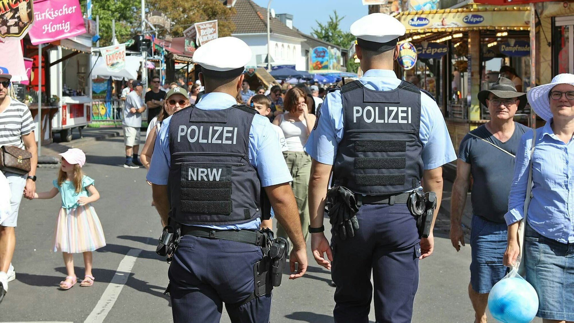 Zwei Polizisten gehen über eine Straße auf der Kirmesbuden stehen.