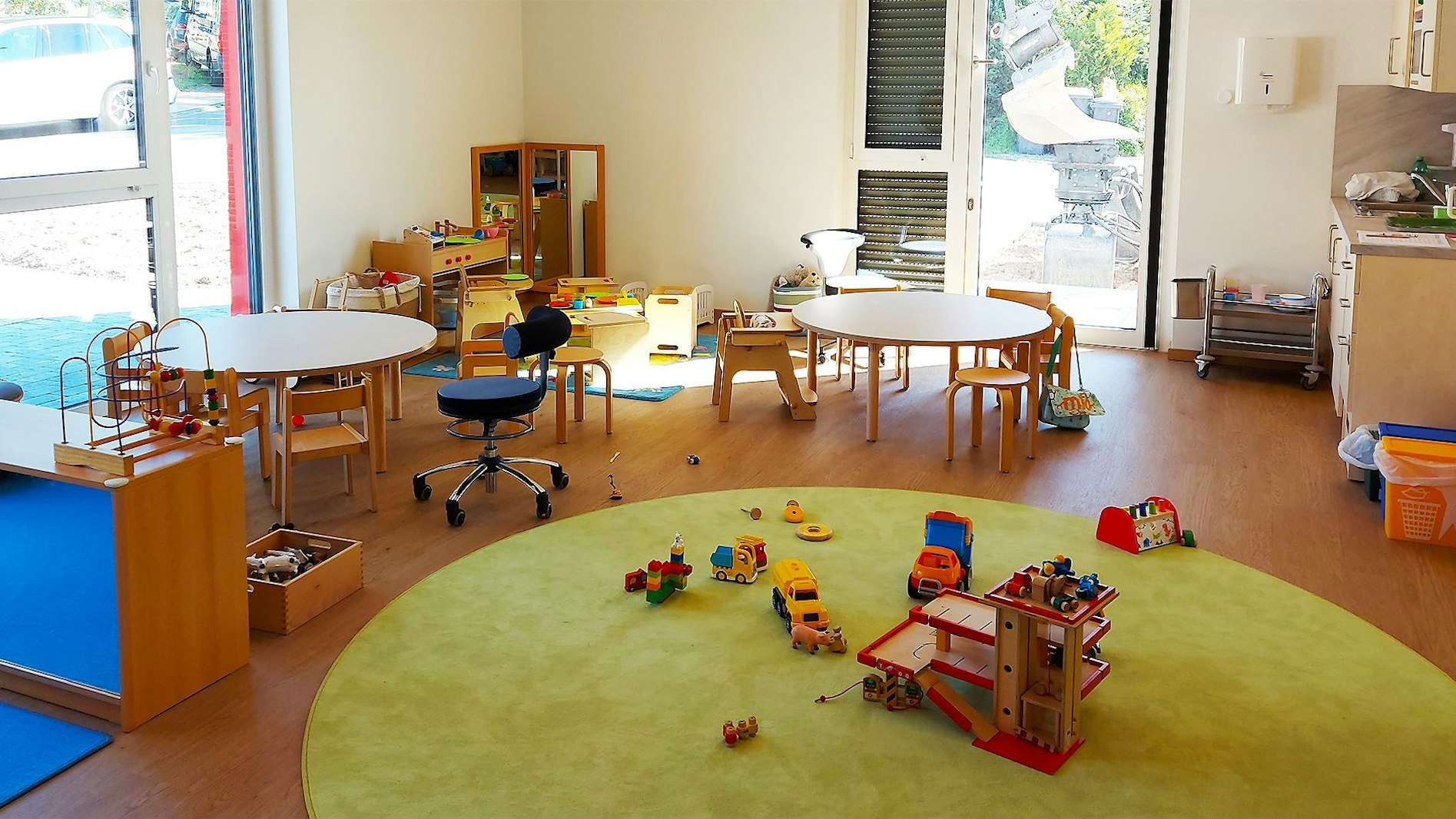 Ein Raum mit kindgerechten Tischen und Stühlen und Spielzeug auf einem Teppich ist von innen zu sehen.