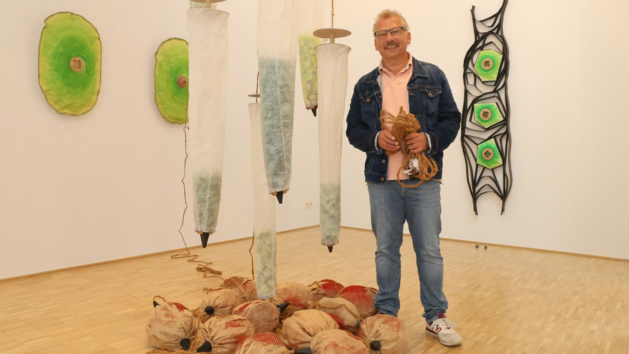 Der Künstler steht neben hängenden Objekten.