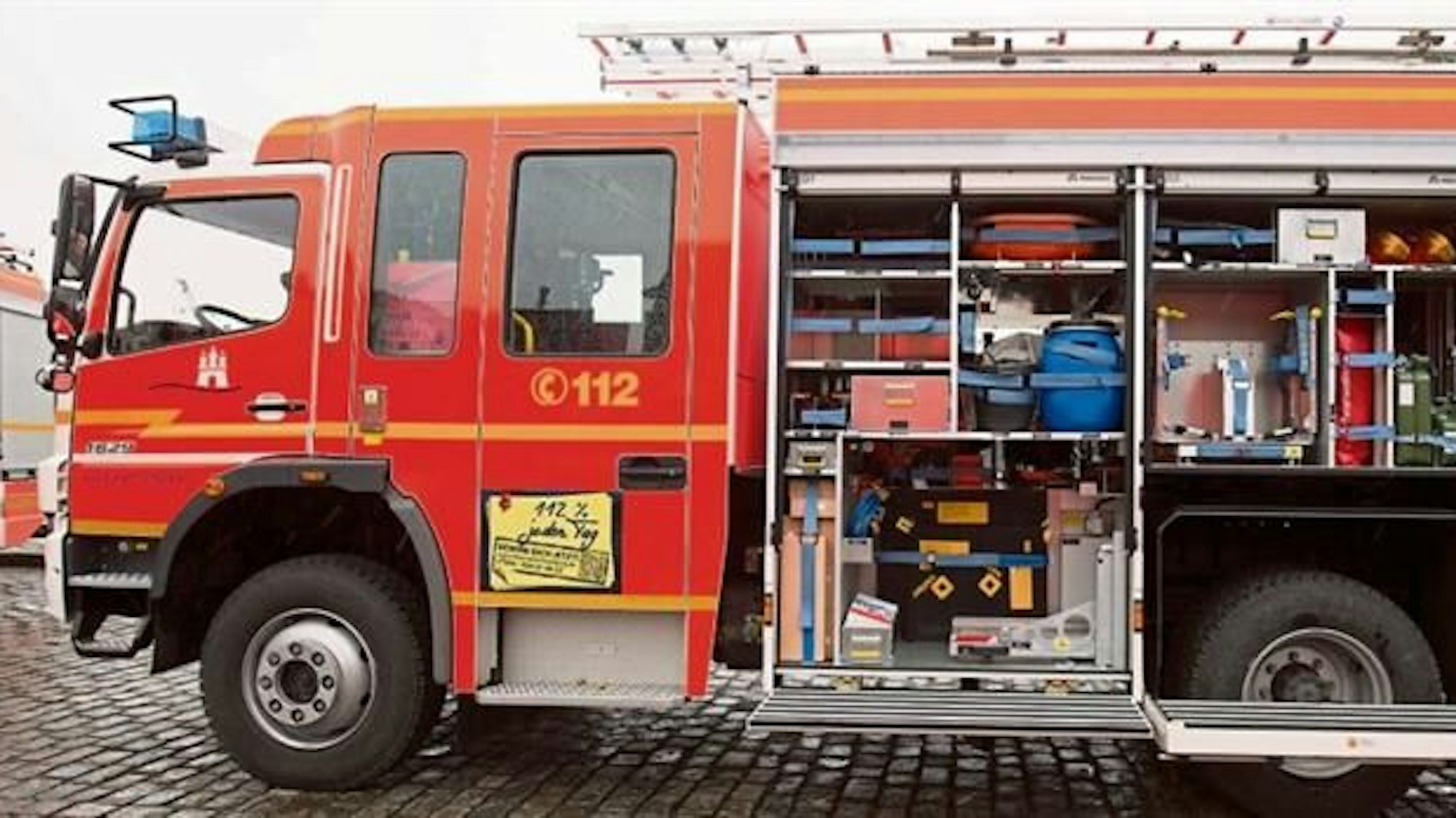 Ein rotes Feuerwehrfahrzeug mit Schiebeleiter auf dem Dach und geöffnetem Materialfach.