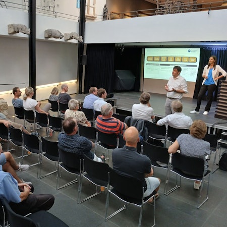 Menschen auf Stühlen bei einer Informationsveranstaltung.