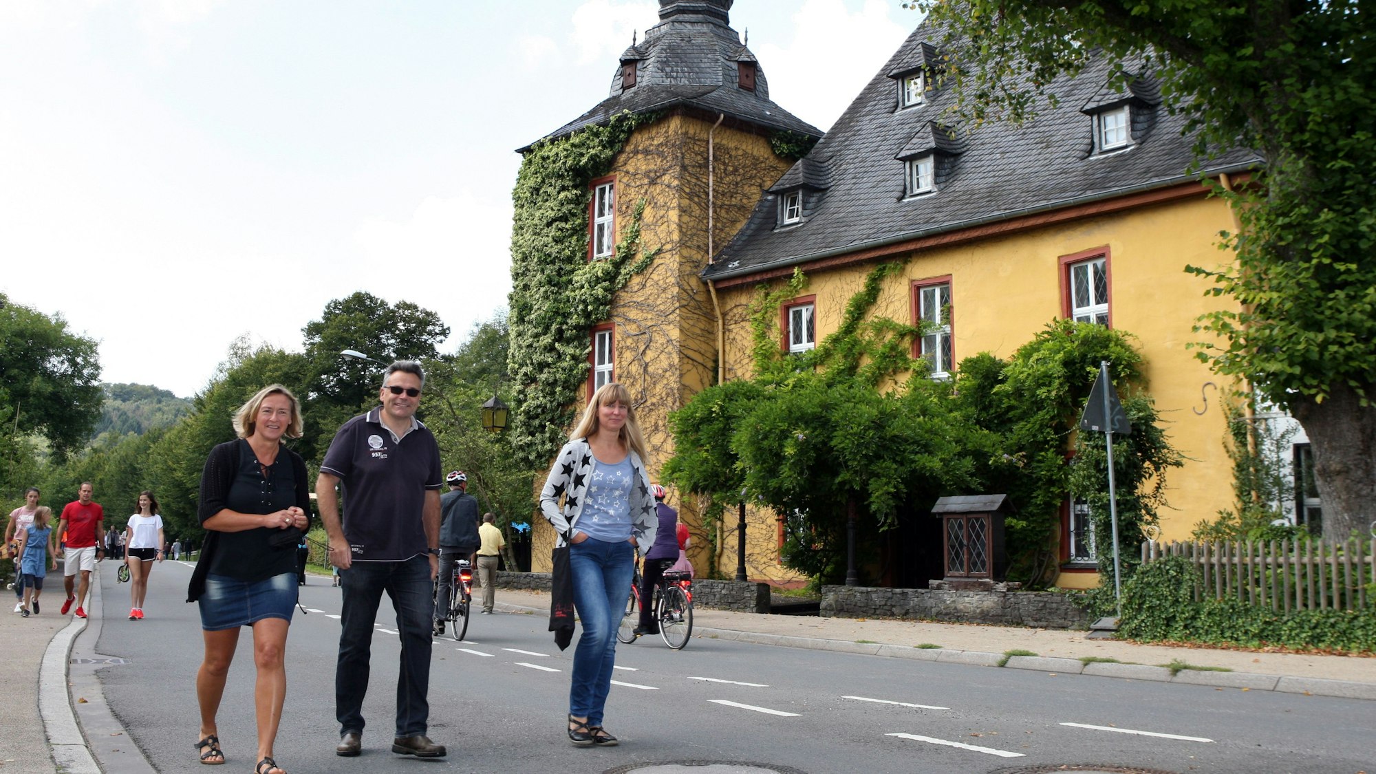 Menschen gehen auf der Landstraße vor Burg Zweiffel in Bergisch Gladbach-Herrenstrunden beim Strundetal-Fest.