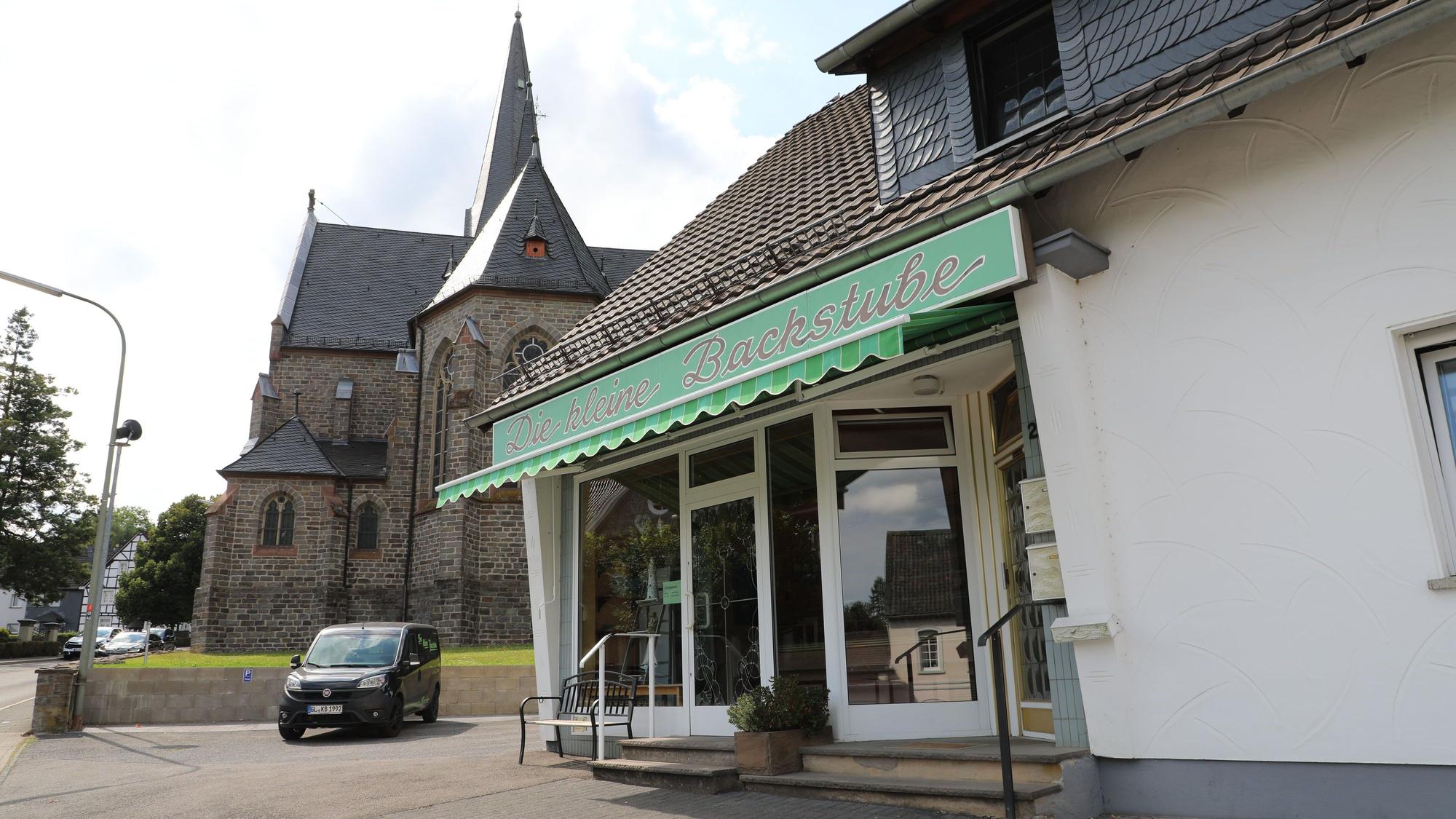 Vor einer Kirche ist ein Laden mit der Aufschrift „Die kleine Backstube“ im Ortskern von Kürten-Olpe zu sehen.