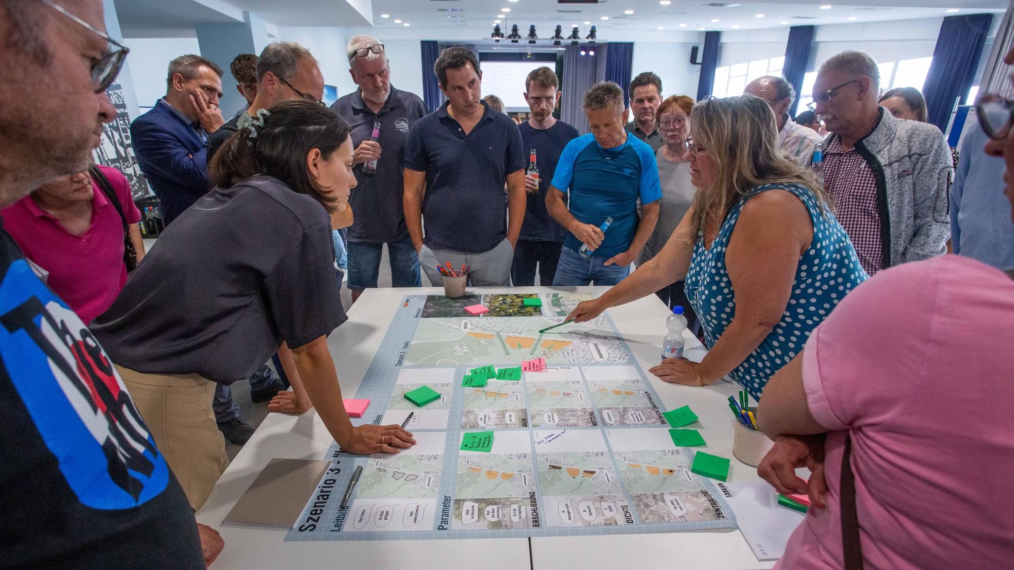 Menschen beugen sich über auf einem Tisch ausgebreitete Pläne.