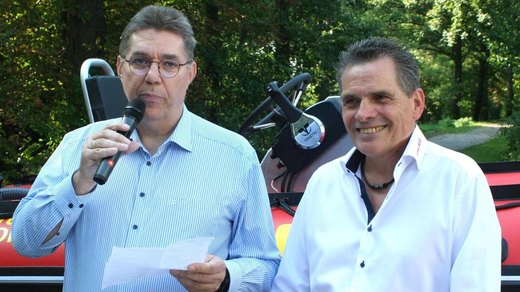 Zwei Männer im Hemd, einer spricht in ein Mikrophon.