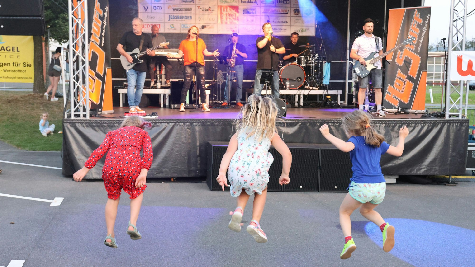 Drei Kinder hüpfen vor der Bühne des Open-Air-Konzerts zum Feuerwehrjubiläum in Wiehl Marienhagen.