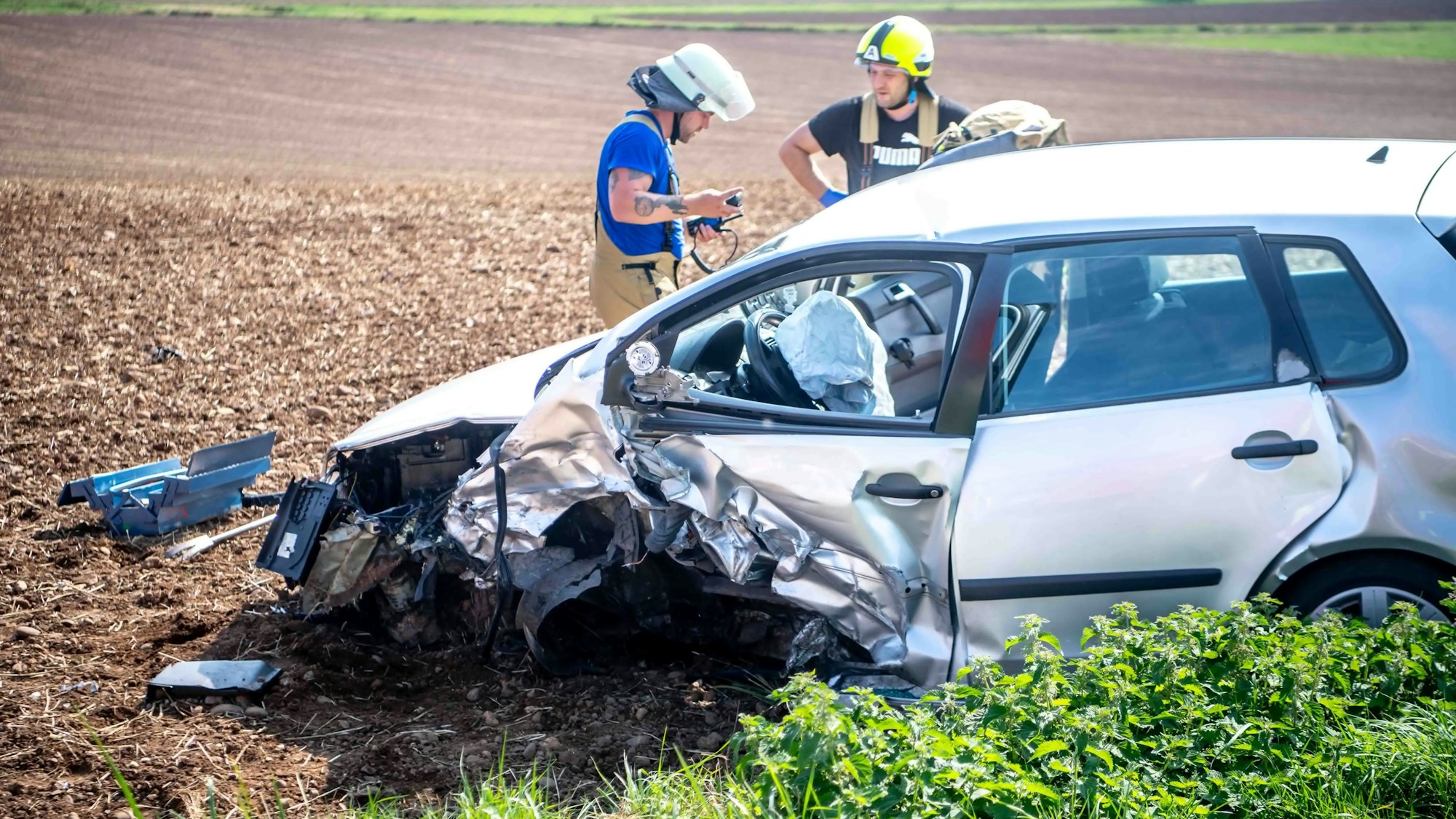 Ein demolierter Wagen steht im Feld, dahinter sind Einsatzkräfte zu sehen.