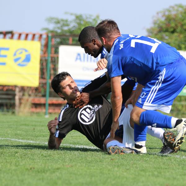 Ein Fußballspieler, der auf dem Boden liegt, und zwei Gegenspieler befinden sich in einer Auseinandersetzung.