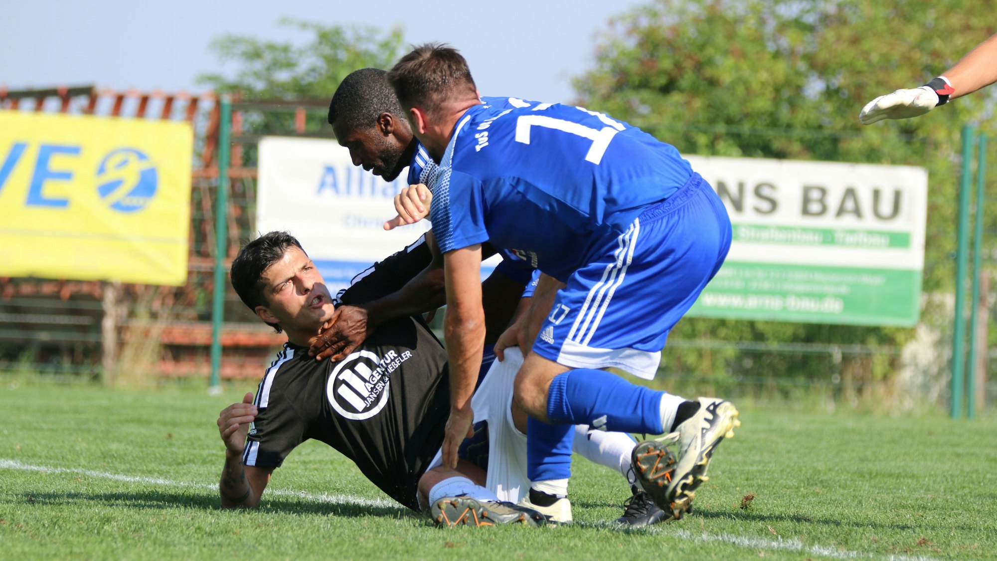Ein Fußballspieler, der auf dem Boden liegt, und zwei Gegenspieler befinden sich in einer Auseinandersetzung.