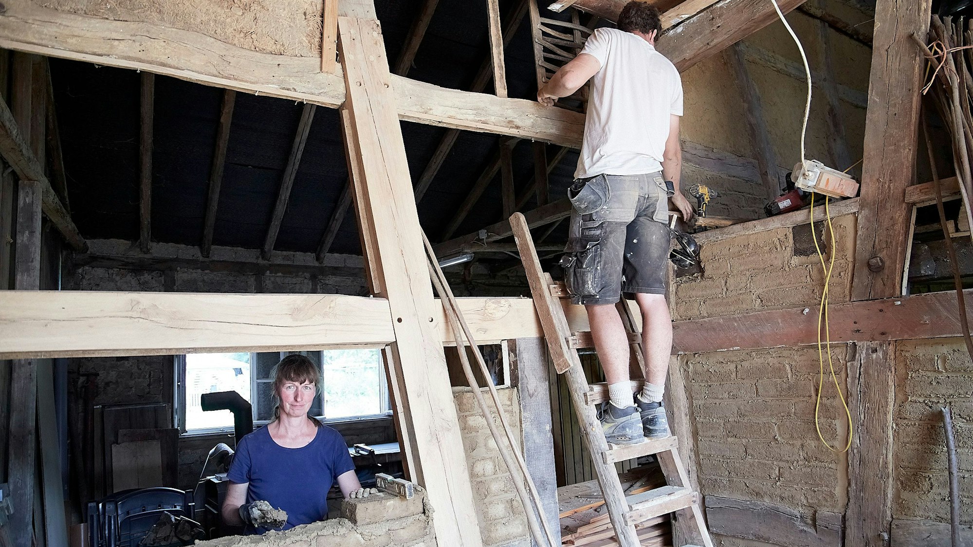 Das Bild zeigt die neue Hausbesitzerin, wie sie eine Fachung mauert. Luca Hickel steht auf einer Leiter.
