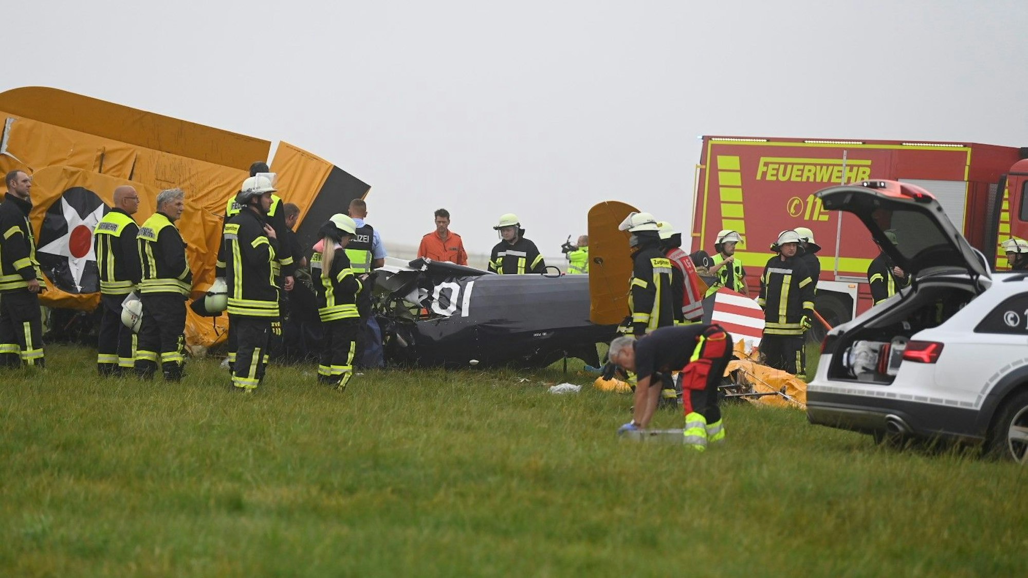 Das Wrack des Flugzeugs liegt auf einem Feld, umgeben von Feuerwehrleuten.