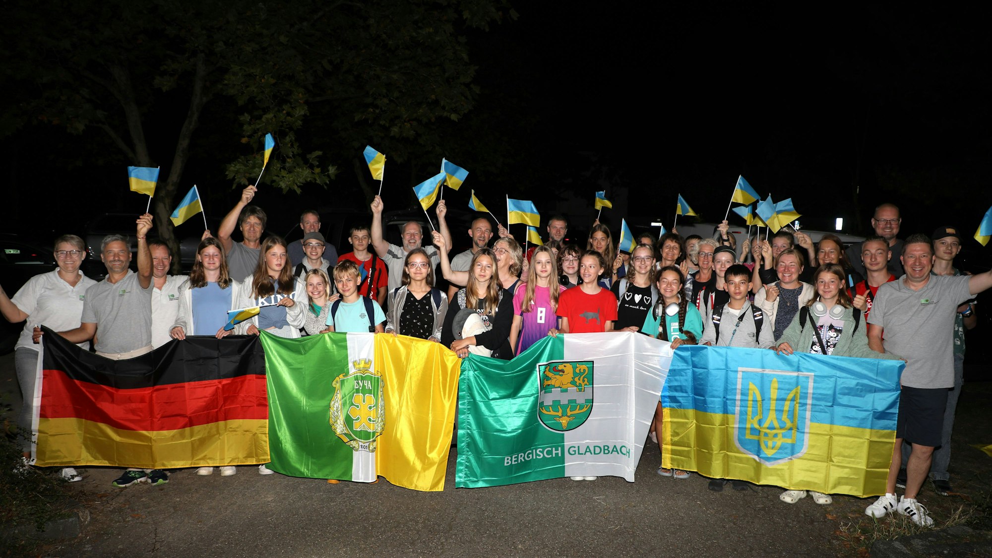 Menschen halten eine ukrainische, eine deutsche sowie die Fahnen von Bergisch Gladbach und Butscha.