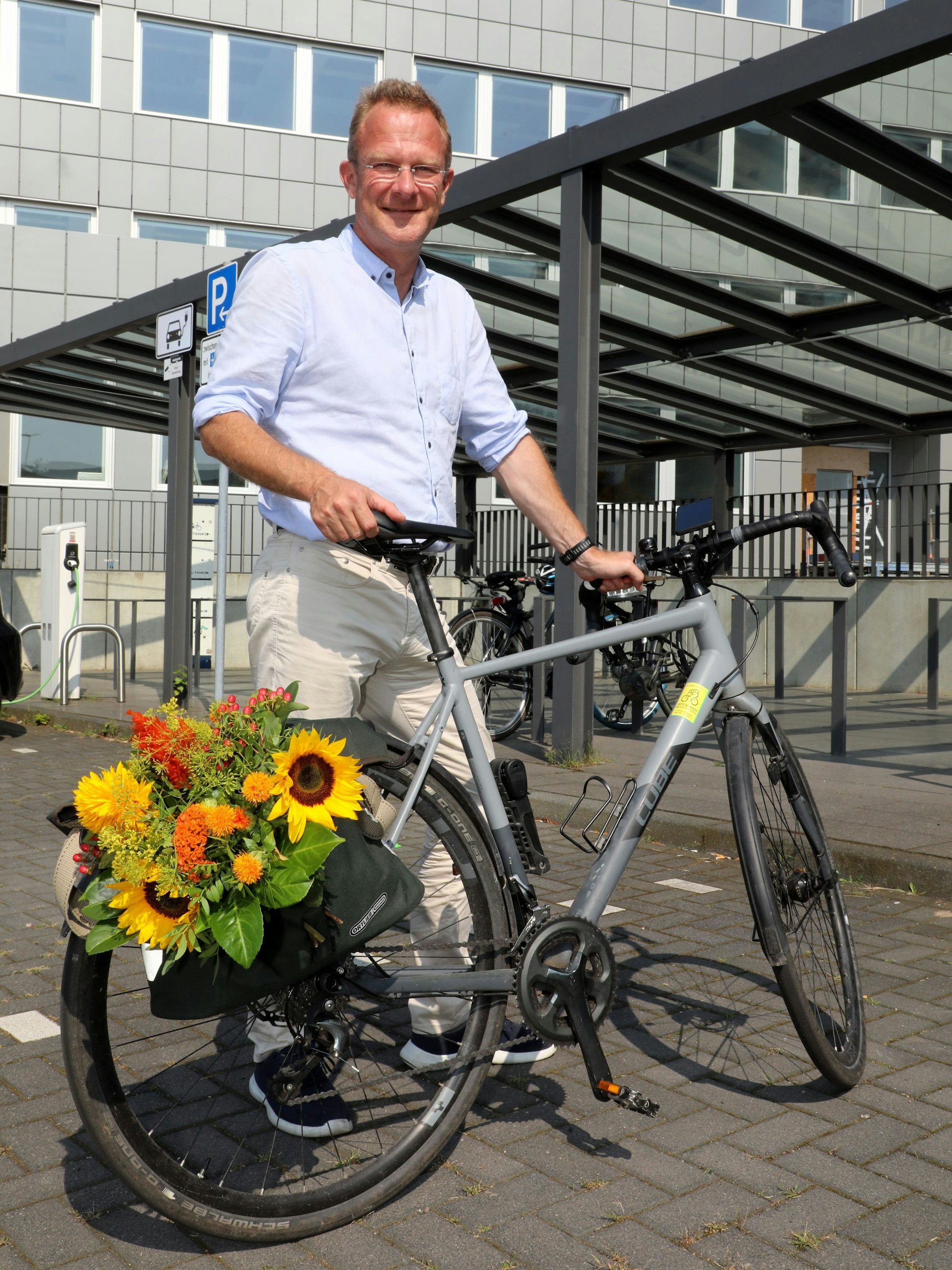 Maik Außendorf hält ein Fahrrad, in dessen Gepäcktaschen einen Blumenstrauß verstaut ist.
