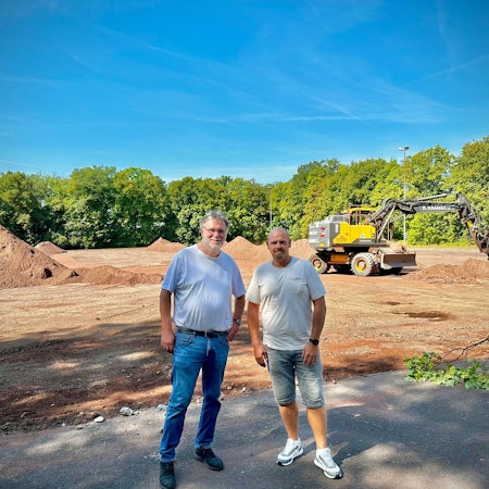 Präsident Hans-Georg Offermann (l.) und Abteilungsleiter Mario Petrovic stehen am Dienstag (27. August 2024) vor dem Sportplatz des RSV Rath-Heumar, der derzeit zum Kunstrasenplatz umgebaut wird.
